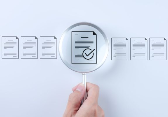 Document review process and quality control concept. Hand holding magnifying glass over a document icon with checklist, Document review and approval. Certificate management, Audit, Standardization,